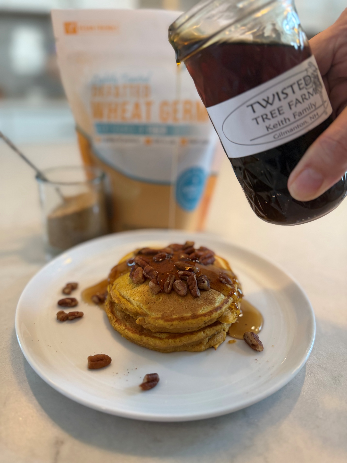 Pumpkin pancakes topped with pecans and maple syrup, with a Viobin defatted wheat germ bag in the background.